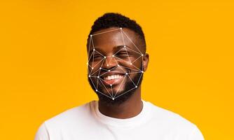 A young man is smiling against a bright yellow background, showcasing facial recognition technology overlay on his features. The image highlights advancements in identification and data processing. photo
