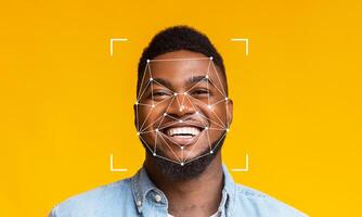 A man is smiling brightly against a vibrant yellow background, showcasing the application of facial recognition technology. Geometric patterns overlay his face to indicate detection. photo