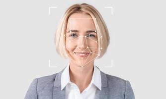 A woman with blonde hair smiles confidently while facial recognition technology analyzes her features. The setting has a light, empty background, emphasizing the subject and technology. photo
