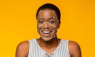 A woman with short hair is smiling while facial recognition technology outlines her features. The bright yellow background enhances the focus on her joyful expression and the tech overlay. photo
