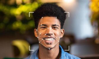 A young man is smiling while facial recognition technology scans his face. This advanced identification method is shown in a modern, well-lit environment with green foliage. photo