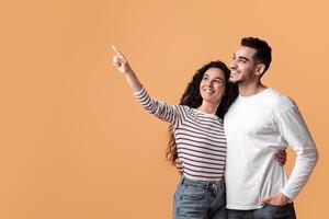 Check This. Smiling Young Middle Eastern Couple Pointing Aside At Copy Space With Finger, Cheerful Arabic Spouses Showing Free Place For Design Or Advertisement On Yellow Background, Panorama photo