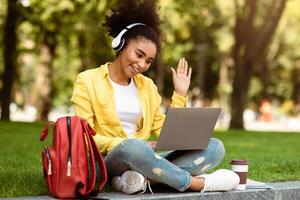 Distance Communication. African American Student Girl Making Call Via Laptop Using Computer For E-Learning Watching Remote Lecture Sitting Outside In Green Park. Modern Online Education photo