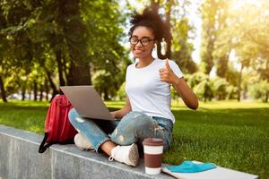 African Student Girl Gesturing Like Posing With Laptop Approving Educational Online Program Or Website Showing Thumbs Up Gesture And Smiling To Camera Outdoor. College Learner Likes E-Learning photo