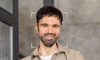 A smiling man stands in a contemporary space with facial recognition markers overlaying his face. This showcases the advancements in identification technology for security purposes. photo