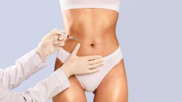Beauty Treatment. Cropped close up front view of young fit woman getting injection in her belly area, having procedure in salon, banner with free copy space. Doctor in gloves making jab in stomach photo