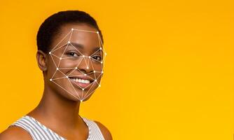 A person smiles as facial recognition technology is applied to their face. The bright yellow background creates a cheerful atmosphere while focusing on the identification process. photo
