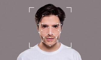 A young man poses against a neutral background while facial recognition technology is applied. The highlights of his facial features are outlined with points and lines, emphasizing identification. photo