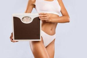 Weight Loss And Control. Unrecognizable young woman holding and showing bathroom scales to measure her weight at home, closeup. Cropped view of millennial lady checking result of her slimming diet photo