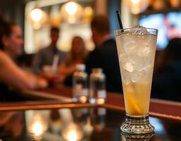 Close-up of a tall glass filled with ice and a light amber-colored drink, garnished with a lemon slice, and a black straw photo