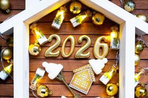 Golden figures number 2026 and tiny background of cozy windows of a house with warm light with festive decor of stars,snow and garlands. Greeting card, Happy New Year, cozy home photo