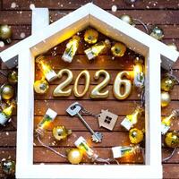 Golden figures number 2026 and tiny home on background of cozy windows of a house with warm light with festive decor of stars,snow and garlands. Greeting card, Happy New Year, photo