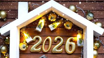 Golden number 2026 and tiny home on background of cozy windows of a house with warm light with festive decor of stars,snow and garlands. Greeting card, Happy New Year, cozy home photo