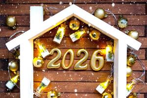 Golden figures number 2026 and tiny home background of cozy windows of a house with warm light with festive decor of stars,snow and garlands. Greeting card, Happy New Year, cozy home photo