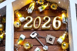 Golden figures number 2026 tiny home on background of cozy windows of a house with warm light with festive decor of stars,snow and garlands. Greeting card, Happy New Year, cozy home photo