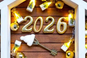 Golden figures number 2026 and home on background of cozy windows of a house with warm light with festive decor of stars,snow and garlands. Greeting card, Happy New Year, cozy home photo