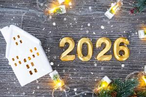New Year 2026 golden numbers and House key tiny form of home on festive grey wooden background flatlay, lights of garlands, greeting card. Housing, real estate, relocation, mortgage, insurance photo