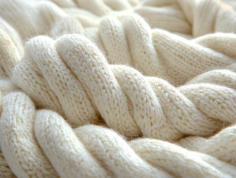 Soft and inviting knitted blanket displays large intertwining loops in warm cream color. natural light enhances cozy texture creating welcoming atmosphere photo