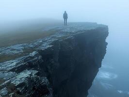 person stands alone on fog covered cliff gazing into endless dark void. setting evokes deep introspection and conveys feelings of existential dread photo