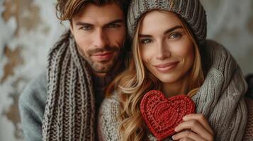 Man and woman stands, dressed in cozy knitted sweaters and scarves, they hold a heart shaped toy. Romantic background for Happy Valentine's Day vibes. photo