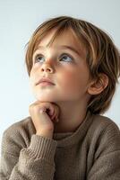 A young boy is looking up with his hand on his chin photo