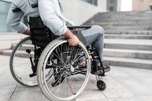 Disability and accessible environment problems. Unrecognizable young black man in wheelchair standing in front of stairs without ramp, having no possibility to enter building, free space photo