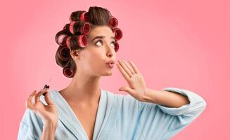 Manicure. Glamorous Housewife With Curlers Blowing At Polished Nails Standing Over Yellow Background. Studio Shot photo