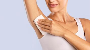 Hyperhidrosis Concept. Closeup cropped view of young lady wiping her under arm area with napkin towel, rubbing armpit isolated on blue studuo background, putting hand up, touching axilla. Perspiration photo