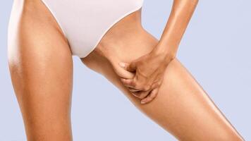 Skin Elasticity Check Concept. Closeup cropped view of unrecognizable young woman pinching her inner thigh, examining cellulite, wearing white panties isolated over blue studio background, banner photo