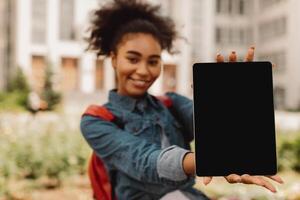 E-Learning. African American Student Girl Showing Digital Tablet With Blank Screen Advertising Educational Website Smiling To Camera Standing Outdoors. Mockup, Selective Focus On Computer photo