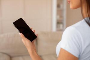 Unrecognizable Girl Holding Phone With Blank Screen Using Mobile Application At Home. Mockup, Cropped, Selective Focus photo