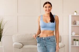 Weight Loss. Happy Girl Wearing Too Big Jeans After Slimming And Dieting At Home. Free Space For Text photo