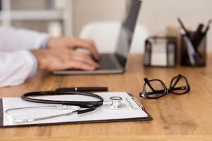Telemedicine Concept. Close up side view of clinician using computer, typing on keyboard, focus on medical equipment photo