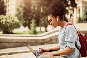 Distance Learning. Happy African American Student Browsing Internet On Laptop Having Remote Lecture Sitting Outdoors. College Girl Using Computer. E-Learning, People And Gadgets photo