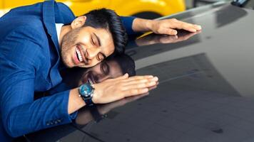 Delighted arab man in stylish suit hugging car of his dream, closing eyes and smiling, closeup, side view, copy space. Happy middle-eastern guy found his auto, visiting automobile salon photo
