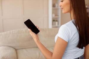 Woman Holding Smartphone With Empty Screen Browsing Internet At Home. Mockup, Selective Focus photo