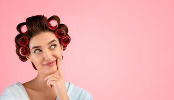 Great Idea. Pensive Housewife With Hair Curlers Smiling Thinking About Something Holding Finger Near Mouth And Looking Aside Posing On Yellow Studio Background. Free Space For Text photo