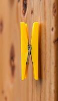A solitary yellow clothespin clinging to a rustic wooden surface creates a simple still life scene photo
