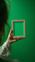 Hand holding picture frame with green screen on a plain green background photo