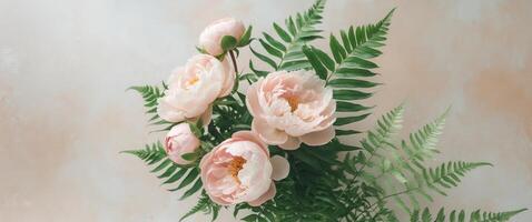 Floral composition featuring delicate pink peonies and fresh green fern leaves on a light textured background with ample space for text. photo