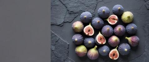 Top view of fresh figs in varying shades of purple and green leaves on dark grey textured background with ample copy space on the left side photo
