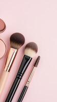 Makeup brushes, lipstick, highlighter, and blush scattered artfully on soft pink representing modern beauty product arrangement Copy space for text photo