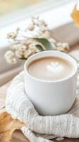 Cappuccino with delicate leaf pattern resting on knitted sweater beside scattered autumn leaves and dried florals, embodying seasonal comfort photo