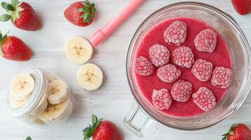 Frozen raspberries, food strawberries and banana slices on wooden table, preparing a healthy smoothie with blender and reusable straw top view photo