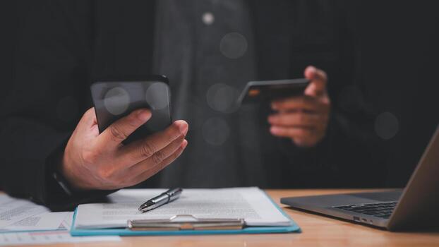 Professional reviews financial information while using smartphone and credit card, highlighting integration of technology in managing personal finances and transactions efficiently photo