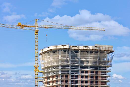 Construction with the help of a tower crane of the top of a multi-storey residential building using a monolithic-frame method against a blue cloudy sky. photo