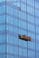 Builders in red overalls are mounting the glass facade of a multi-storey building on a suspended cradle. photo