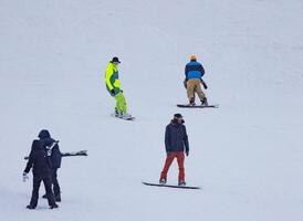 A group of people are riding snowboards down a snow-covered hill. photo