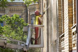 trabajador utilizando un levantar a limpiar el exterior paredes de un histórico edificio debajo un claro azul cielo foto