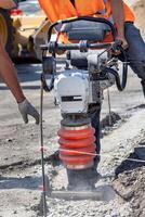 Construction workers using a compactor to prepare ground for building site in bright sunlight photo
